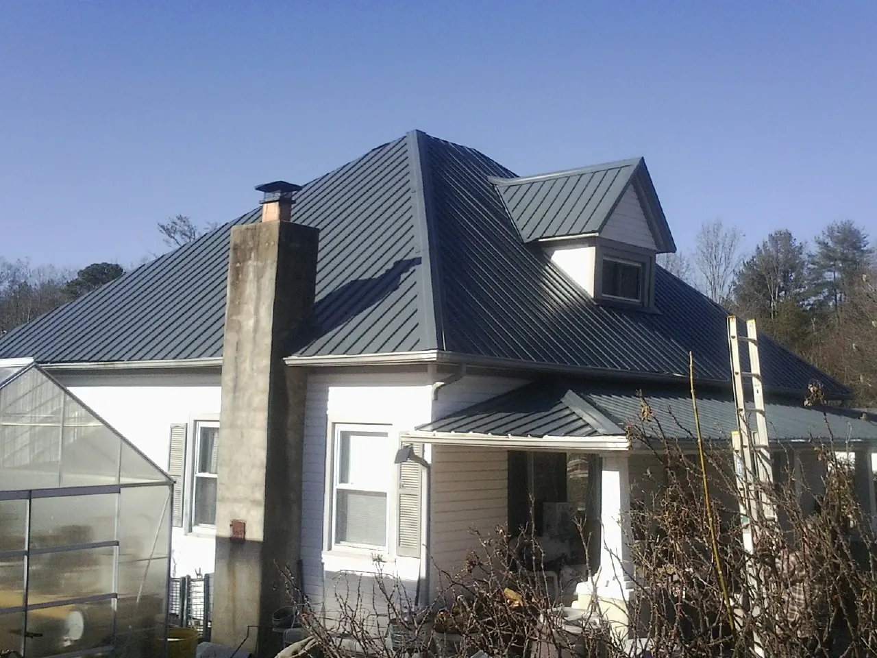 Dark blue standing seam metal roof on a white farmhouse with dormer — Slate & Tile Roof Repair by Roofing Brothers in Foxhome