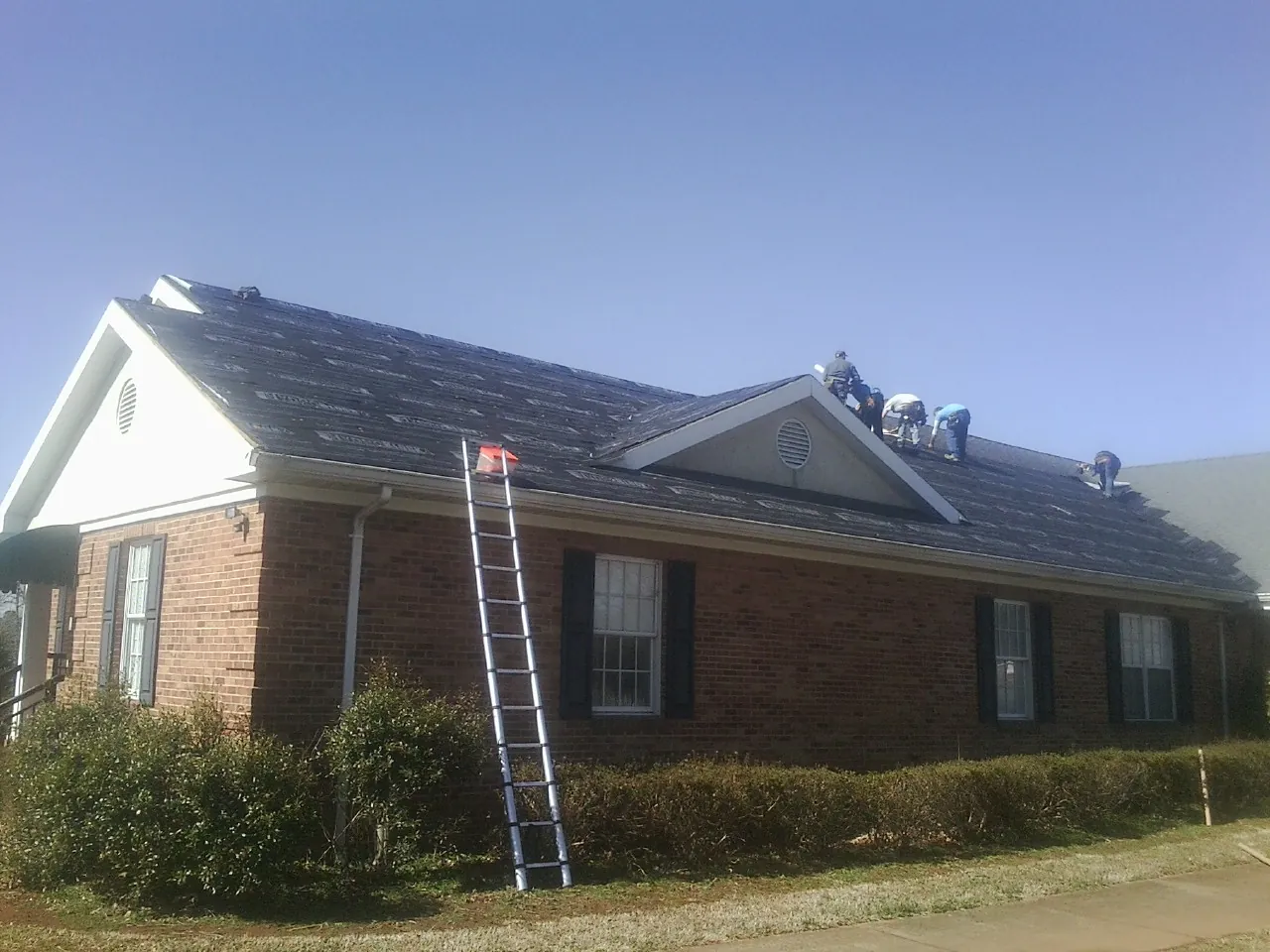 Crew tearing shingles off a brick ranch roof with a ladder set — Emergency Roof Repair work by our crew in Foxhome