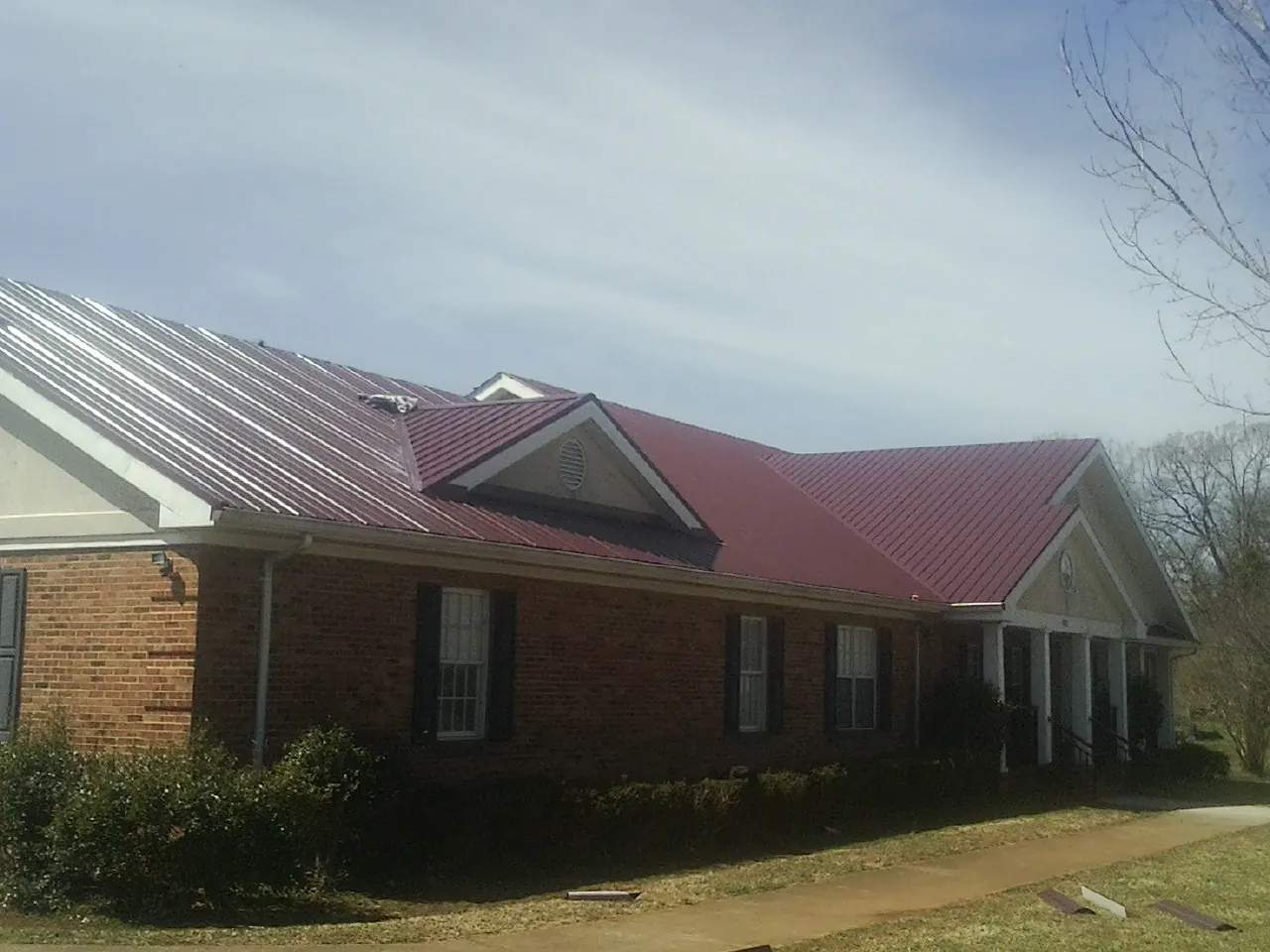 Red metal roof with gabled entries on a long brick building, from a Hail Damage Roof Repair job in Foxhome