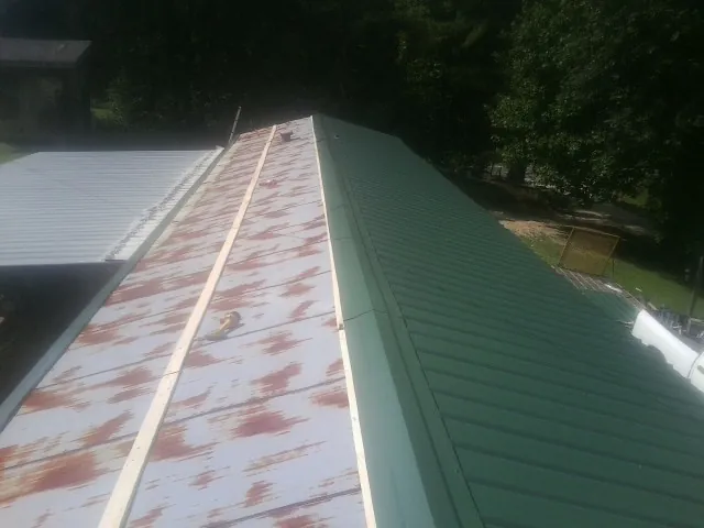 Old rusted panels beside newly installed green metal roofing — Wind Damage Roof Repair by Roofing Brothers in Foxhome
