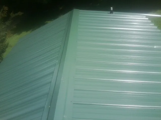 New green metal panels meeting at the ridge of a roof — Flat Roof Repair work by our crew in Foxhome