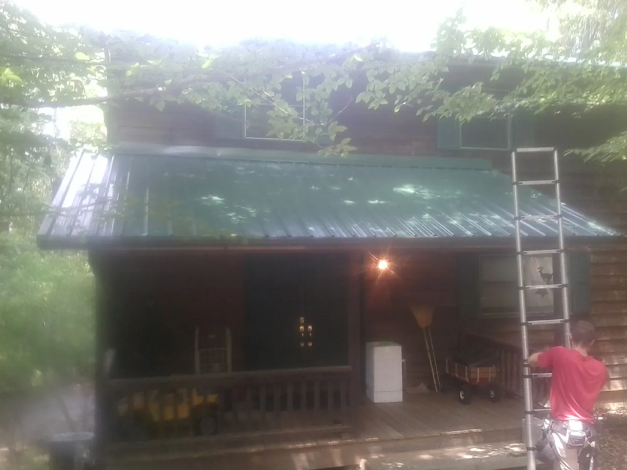 Worker on a ladder at the green porch roof of a wooded cabin in Foxhome