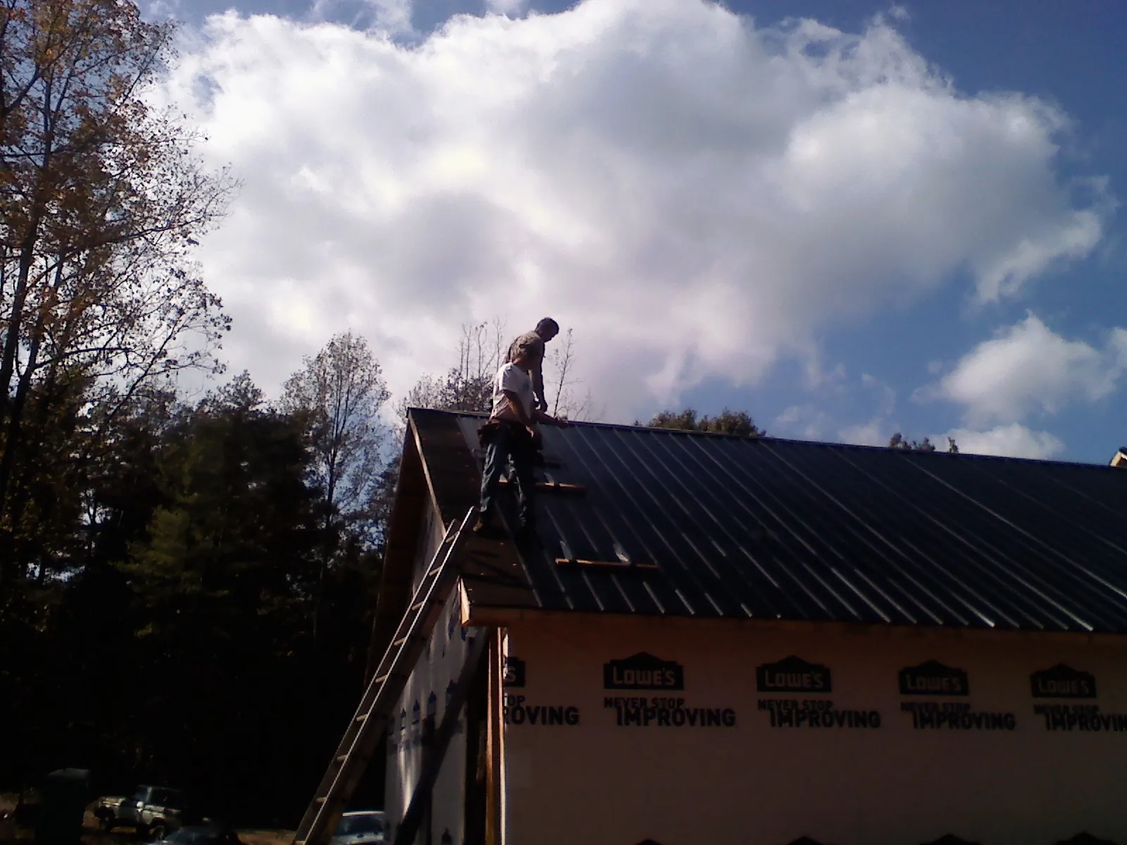 Roofer fastening dark metal panels high against a cloudy sky, from a Roof Inspection job in Foxhome