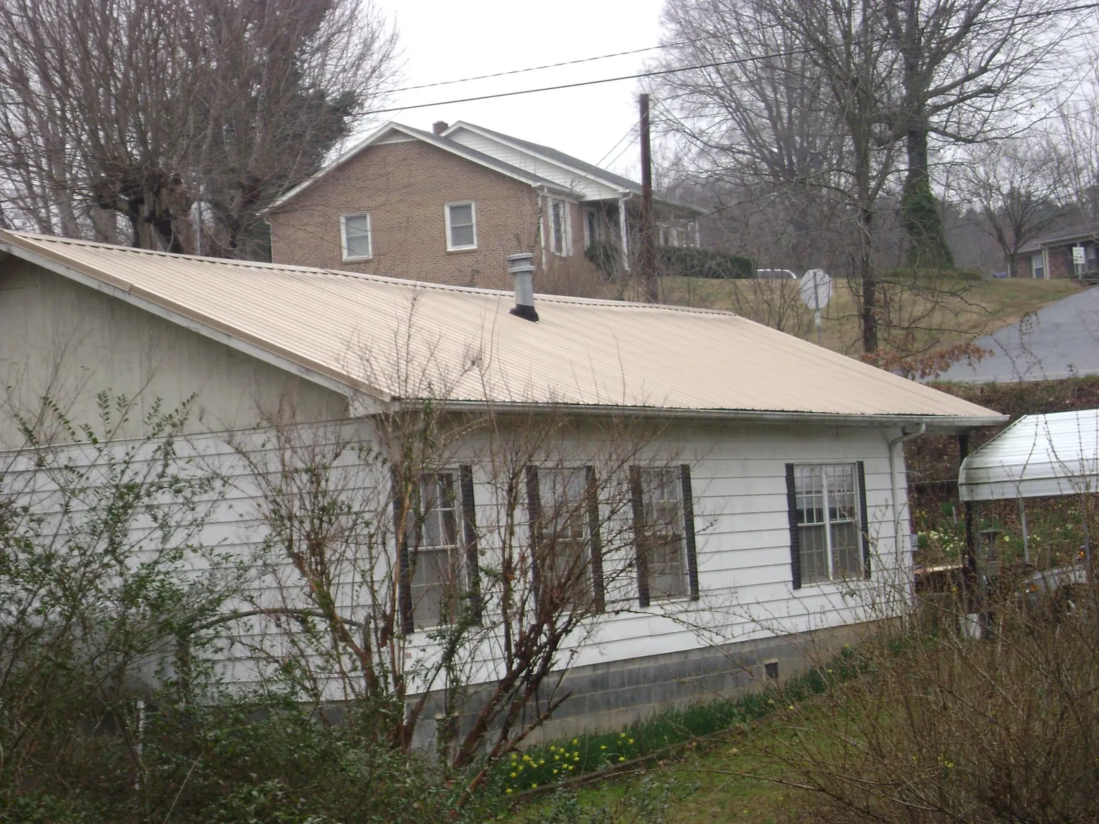 Tan metal roof on a white sided house set into a hillside — Commercial Roofing by Roofing Brothers in Foxhome