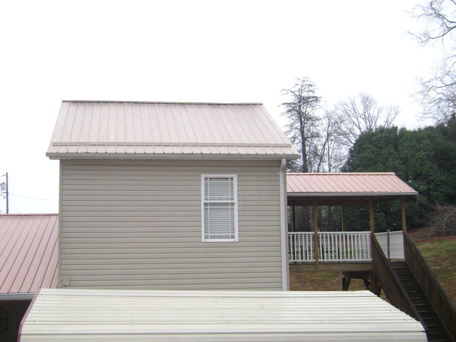 Tan metal roofs on a two story addition and attached porch, from a Roof Replacement job in Foxhome